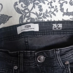 Svarta jeans från FSBN - Säljer ett par svarta jeans från FSBN i modellen 29/30. Jeansen har klassisk femficksdesign, knapp och dragkedja framtill samt bälteshällor. Snygg tvättad look som passar till många stilar.