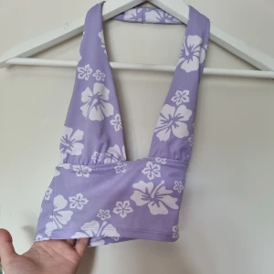 Lila blommig bikiniöverdel - Säljer en lila bikiniöverdel med vita blommor. Fungerar även som en vanlig tröja. Ganska stretchig. Helt ny, har bara provat den nån gång. Står att den är XXS men känns mer som XS.