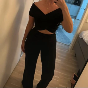 Svart omlott topp med offshoulder jumpsuit Nelly  - Snygg svart omlott topp med offshoulder och v-ringad hals. Toppen har en croppad passform och är perfekt för att skapa en stilren look. Passar till middag, fest, kontor. Jättesnygg passform passar s-m 