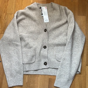 Beige kofta med knappar från Uniqlo - Mysig beige kofta från Uniqlo i mjuk ullblandning. Tröjan har långa ärmar, två framfickor och stängs med tre knappar framtill. Perfekt för lager-på-lager och enkel att matcha med olika outfits.