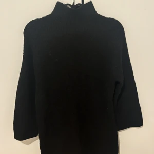 Svart stickad tröja från Stockh lm Studio - Mysig svart stickad tröja från Stockh lm Studio med hög hals och trekvartsärm. Perfekt för kyliga dagar och enkel att matcha med olika outfits.