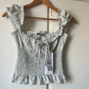 Ljusgrön topp från Gina Tricot - Supersöt grön croppad topp från Gina Tricot med volangdetaljer vid axelband och nederkant. Smockad midja och knyt framtill. Aldrig använd🌸