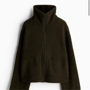 HM Mörkgrön teddyjacka  - Mysig mörkgrön teddyjacka med hög krage och hel dragkedja framtill. Jackan har två stora fickor och en avslappnad passform. Perfekt för kyliga dagar när du vill vara både varm och snygg.