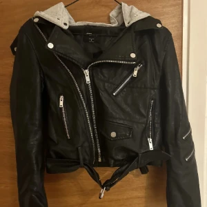 Skinnjacka - En svart skinnjacka med luva. Saknas en knapp som kan ses på bild 3, men fin ändå!💕 Använd 1 gång!