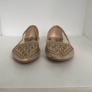 Glittriga ballerinaskor i guld med nitar - Snygga ballerinaskor i guld med spetsig tå och dekorerade med små nitar framtill. Skorna har en platt sula och är perfekta för dig som vill sticka ut lite extra. Lätta att matcha till olika outfits.