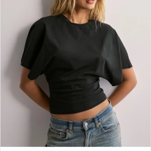 Svart croppad topp med vida ärmar - Snygg svart croppad topp med rund halsringning och vida korta ärmar. Perfekt till jeans eller kjol för en trendig look. Toppens material ser ut att vara mjukt och stretchigt.