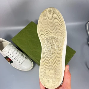 Gucci Ace vita sneakers med röd/grön detalj - Gucci Ace sneakers i vitt skinn med klassiska gröna och röda sidband samt metallicröd och metallicgrön häl i ormskinnslook. Snygg broderad guldbi på sidan och platt sula med unikt mönster undertill. Kommer med originalkartong.