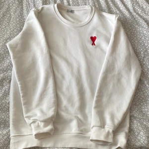 Vit sweatshirt från Ami Paris med rött hjärta - Vit sweatshirt från Ami Paris med broderad röd hjärtlogga på bröstet. Klassisk rund halsringning och långa ärmar med muddar. Tillverkad i mjuk bomull för en skön och avslappnad look. Pris kan diskuteras!!