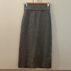 Grå stickad långkjol från H&M - Mysig grå stickad långkjol från H&M med ribbade detaljer i midjan och nederkant. Kjolen har en liten slits bak för extra rörelsefrihet och är perfekt för dig som gillar en chill och stilren look.