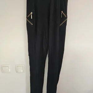 Svarta byxor Chiara Forthi med dragkedjor - Svarta byxor från Chiara Forthi med snygga guldfärgade dragkedjor framtill. Byxorna är tillverkade i mjuk bomull med stretch för skön passform. De har en smal siluett och passar perfekt till en trendig streetstyle-look.