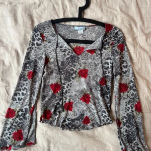 Grå mesh topp med rosor från Request - Supersnygg mesh topp från Request med grått leopardmönster och röda rosor över hela. Långärmad med v-ringning och tunna knytband framtill. 