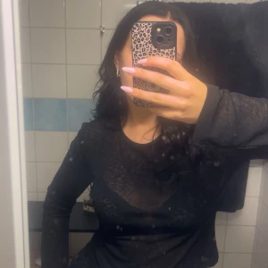 Svart mesh topp från Nelly - Säljer en svart mesh topp från Nelly i storlek M. Toppen är långärmad och har en transparent look som ger en edgy vibe. Perfekt att styla med coola accessoarer eller lager på lager. Passformen är normal och materialet känns lätt och syntetiskt.