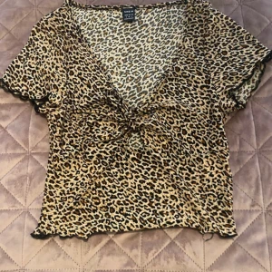 Leopardmönstrad crop top från SHEIN - Säljer en leopardmönstrad omlottopp från SHEIN i storlek S. Toppen har korta ärmar, v-ringning och en snygg knytning framtill. Materialet är mjukt och stretchigt, perfekt för att sticka ut med ett djurmönster. Passar dig som gillar trendiga och djärva plagg.