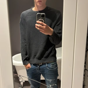 Mörkgrå stickad tröja från John Baner - Säljer en mörkgrå stickad tröja från John Baner med diskret struktur och rund hals. En broderad logga på vänster arm som är snygg. Tröjan är riktigt skön och sitter bra.