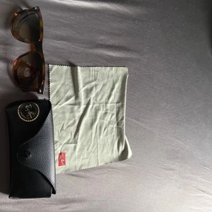Ray-Ban Boyfriend solglasögon - Säljer ett par snygga Ray-Ban boyfriend solglasögon med brun transparent båge och mörka glas. Medföljer original svart fodral i skinnimitation och putsduk med Ray-Ban logga. Perfekt accessoar för soliga dagar och stilrena outfits.