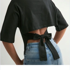 Svart croppad topp med knyt i ryggen från nelly - Svart croppad topp med halvlånga ärmar och öppen rygg som knyts med en stor rosett baktill. T-shirten har en cool och modern look, perfekt för att sticka ut. Tillverkad i mjukt bomullstyg som känns skönt mot huden.