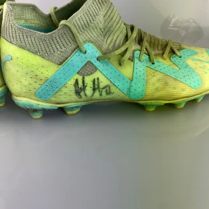 Puma fotbollsskor i limegrönt och turkos - Säljer ett par snygga Puma fotbollsskor i limegrönt med turkosa detaljer och logga. Skorna har snörning, stickad strumpliknande krage och platt sula med dobbar för gräsplan. Perfekta för dig som vill sticka ut på planen!