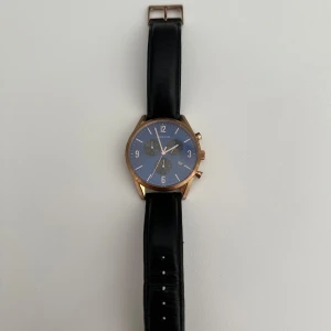 Bering klocka med svart läderband - Stilren klocka från Bering med svart läderarmband och blå urtavla. Boetten är i roséguld och har tre mindre urtavlor samt datumvisning. Klockan har en klassisk rund form och detaljer i guldton. 