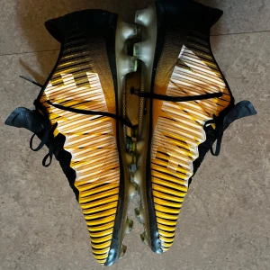 Nike Mercurial vapor 11 - Snygga Nike Mercurial fotbollsskor i svart och gult med coolt randigt mönster och stora vita swoosh-loggor. Skorna har snörning och platt sula med dobbar för gräsplan. Ovandelen är i syntetmaterial för bästa bollkontroll och passform. Ganska sällsynt färg 