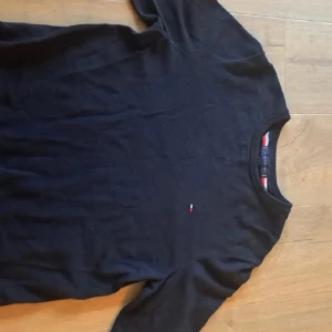 Tommy Hilfiger stickad tröja sweatshirt - Klassisk svart stickad tröja från Tommy Hilfiger i storlek L. Tröjan har rund halsringning, diskret logga broderad på bröstet och ribbade muddar. Perfekt för dig som gillar stilren och enkel design med en touch av premiumkänsla. Nypris runt 1300kr använda endast 2 gånger, det är storlek L men passar nog mer M beroende på kroppsform