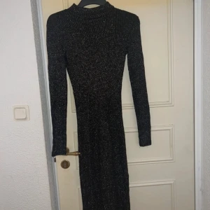 Svart glittrig långklänning med polokrage - Säljer en svart långklänning med glittriga detaljer och polokrage. Klänningen är ribbad och har lång ärm, vilket ger en slim och snygg siluett. Perfekt för dig som vill sticka ut med lite extra glitter. Passar dig som gillar stilrena och trendiga plagg.
