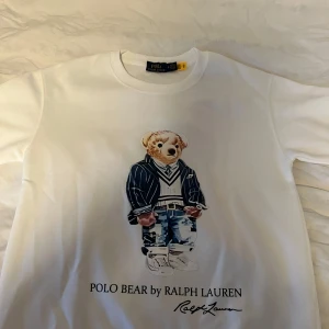 Vit långärmad Polo Bear sweatshirt - Vit långärmad t-shirt från Polo Ralph Lauren med ikoniskt Polo Bear-tryck framtill. Klassisk rund halsringning och relaxed fit. Perfekt statement-plagg för dig som gillar streetstyle och preppy vibes. Tröjan är helt ny har bara testat den men den passade ej eftersom den var för liten. Pris kan diskuteras.