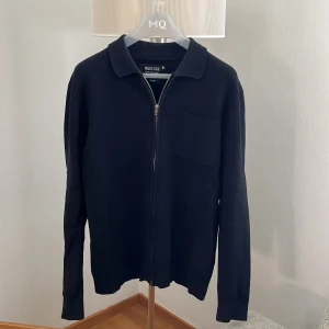 Svart kofta med dragkedja från Indicode - Svart kofta från Indicode i storlek Large. Klassisk design med krage, hel dragkedja framtill och en bröstficka. Materialet är mjukt och känns skönt mot huden, perfekt för lager-på-lager. Passformen är normal och ärmarna är långa.