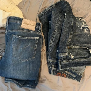 Två par blå jeans Jacob Cohen - Säljer två par snygga blå jeans från Jacob Cohen. Ena paret är klassiskt blått med diskreta slitningar, det andra har mer slitna detaljer och patchar. Båda har femficksdesign och tydliga kontrastsömmar. Perfekta för dig som gillar en avslappnad men trendig look.