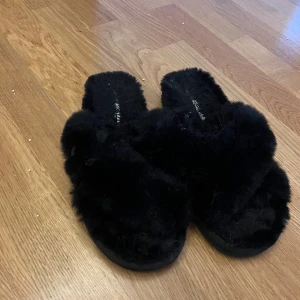 Svarta fluffiga sandaler Michael Kors - Svarta sandaler från Michael Kors med mjuk, fluffig pälsimitation över foten och platt sula. Snyggt MK-emblem på sidan och ribbad undersida för extra grepp. Perfekta för att chilla hemma eller ge din outfit en cozy vibe.