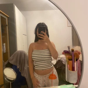 Randig bandeau tubtopp från H&M - Säljer en ribbad bandeau tubtopp från H&M i vitt med svarta horisontella ränder. Toppen är ärmlös och axelbandslös, perfekt för varma dagar. Den har en slim passform och är superenkel att styla med jeans eller kjol. Köpt för 180 kr.