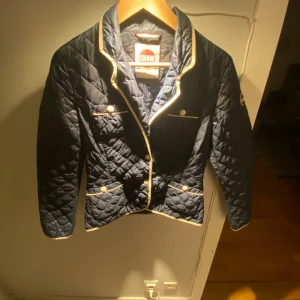 Mörkblå  jacka från Colmar - Snygg mörkblå quiltad jacka från Colmar med vita detaljer och knappar. Jackan har lång ärm, markerad krage och fyra fickor framtill. Perfekt för dig som gillar stilren och sportig look. Klassisk logga på ärmen och insidan.🙌🙌💠 det passar från 160-170