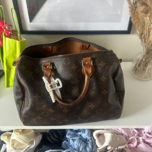 Louis Vuitton handväska Speedy - Säljer en klassisk brun handväska från Louis Vuitton med ikoniskt monogrammönster och detaljer i ljusbrunt skinn. Väskan har två handtag och dragkedja upptill, perfekt storlek för att få plats med allt du behöver. Den är nästan nyköpt från Soleplus och äkthetbevis finns. Det är inga tydliga defekter eller liknande. Skriv privat vid frågor, fler bilder osv💗💗