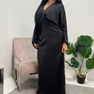 Svart långklänning med knyt i midjan - Säljer en svart långklänning med v-ringning och långa ärmar. Klänningen har ett snyggt knyt i midjan. Materialet är mjukt och har en lätt glansig finish liknande satin. Onesize men skulle säga att den passar från S-L då den går att justera i midja så man önskar men ändå är lös i passform. Köpt för ca 400kr, aldrig använd bara testad. 