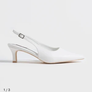 Helt nya vita pumps med spetsig tå och låg klack - Snygga vita pumps med spetsig tå och låg klack. Skorna har en öppen häl med justerbart spänne och en elegant siluett. 