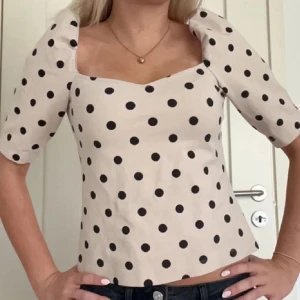 Prickig beige blus med puffärm - Superfin beige blus med svarta prickar och trendiga puffärmar. Snygg fyrkantig urringning och lätt figursydd passform. Perfekt att styla med jeans eller kjol för en cool look.