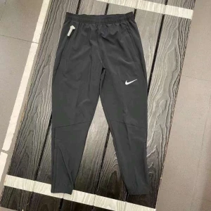 Svarta träningsbyxor från Nike - Snygga svarta träningsbyxor från Nike med vit logga på benet. Byxorna har elastisk midja med snörning och smal passform som sitter skönt. Tillverkade i lätt polyester som andas bra, perfekta för gymmet eller löprundan.