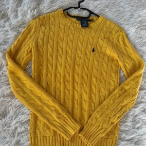 Gul kabelstickad tröja Ralph Lauren - Säljer en snygg gul kabelstickad tröja från Ralph Lauren i 100% bomull. Tröjan har långärmade och ribbade muddar samt det klassiska broderade logot på bröstet. Perfekt för dig som vill ha en färgklick i garderoben!💕