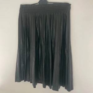 Svart långkjol från Vero Moda - Snygg svart långkjol från Vero Moda med plisserad design och bred resår i midjan. Kjolen har ett stilrent och flowy fall som ger en cool vibe till din outfit. Perfekt att matcha med sneakers eller boots för en trendig look.