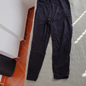 Svart jumpsuit från Gina Tricot, strl 34 - Svart jumpsuit från Gina Tricot i mjukt och lätt material. Modellen har smala ben, v-ringad hals och snygg snörning i ryggen. Perfekt för dig som gillar stilrena plagg med enkel passform och vill ha något som sticker ut med detaljerna i ryggen.