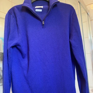 Blå merinoulltröja half zip These Glory Days - Snygg blå tröja i merinoull från These Glory Days. Modellen har half zip-dragkedja och hög krage, perfekt för lager-på-lager. Långärmad och i mjukt, stickat material som känns lyxigt och bekvämt. Passar dig som gillar stilren och enkel design.