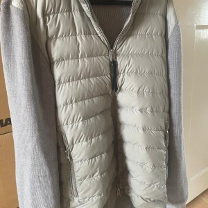 Woolrich grå quiltad cardigan  - Snygg grå woolrich cardigan jacka med quiltad framsida och stickade grå ärmar och rygg. Jackan har två fickor med dragkedja och en hel dragkedja framtill. Perfekt för dig som gillar stilren och grich. Jackan passar även dem som har storlek M ✅💸