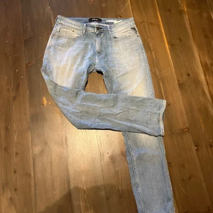 Replay Dave ljusblå jeans comfort fit - Säljer ett par Replay Dave jeans i ljusblå tvätt med comfort fit. Klassisk femficksmodell, raka ben och normal passform. Snygga slitningar framtill och bak, med Replay-logga i midjan. Perfekt för dig som gillar avslappnad stil och vill ha jeans med lite extra attityd.