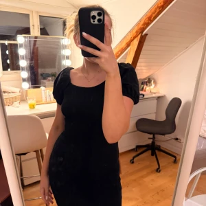 Svart kort klänning Gina Tricot - Supersnygg svart kort klänning från Gina Tricot med puffärmar och smockad kropp. Klänningen har en tight passform och är perfekt om du vill ha en enkel men trendig look. Materialet känns mjukt och stretchigt, vilket gör den bekväm att bära.