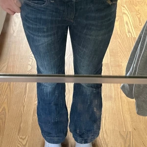 Blå flared jeans från H&M, mid waist - Säljer ett par blå jeans från H&M med flared ben och justerbar midja. Jeansen har klassisk femficksdesign, snygga slitningar och är i mid waist-modell. Perfekta för dig som gillar en retro vibe och vill ha bekväma jeans med lite extra attityd.