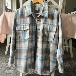 Rutig jacka - Säljer en rutig jacka från Studio i mjukt material. Skjortan har blå, beige och vita toner, två bröstfickor med lock och knappar framtill. Använd fåtal gånger 