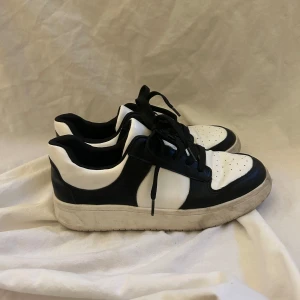 Svarta och vita sneakers med snörning - Säljer ett par svartvita sneakers med klassisk design och snörning från monki. Skorna har rund tå, platt sula och perforerade detaljer framtill i strl 38. 