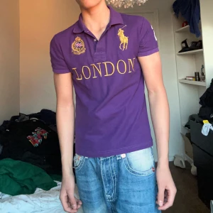 Chief keef polo Ralph lauren  - Säljer en lila pikétröja från Polo Ralph Lauren med stor gul logga och texten LONDON på bröstet. Tröjan har klassisk krage, knappar och stort tryck med siffran 2 på ryggen. Perfekt för dig som gillar sportig och stilren look.