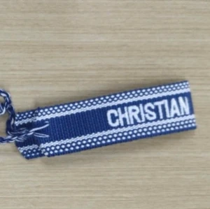 Christian Dior J'ADIOR armband - Säljer ett blått tygarmband från Dior med vit text 'CHRISTIAN DIOR J'ADIOR'. Armbandet har ett flätat avslut och är dekorerat med vita detaljer längs kanterna. Perfekt accessoar för att lyfta din outfit.