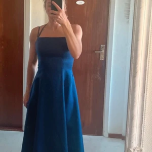 Marinblå långklänning med smala axelband - Säljer en elegant marinblå långklänning med smala axelband och rak urringning. Klänningen har en figurnära överdel och utsvängd kjol, samt öppen rygg med knytband. Perfekt för speciella tillfällen! Balklänning & till stundenten 
