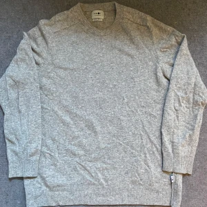 Ljusgrå stickad tröja från NN07 - Säljer en stilren ljusgrå stickad tröja från NN07. Tröjan har rund halsringning, långa ärmar och ribbade muddar vid ärmslut och nederkant. Perfekt för lager-på-lager och enkel att matcha med olika outfits.